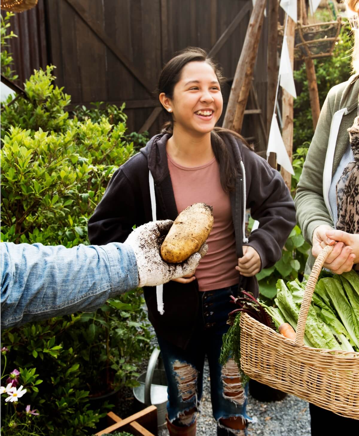 Jeune fille souriante recevant une pomme de terre d'un producteur, à côté d'un panier de légumes frais.