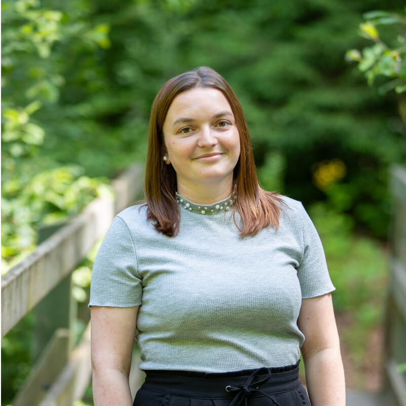 Portrait de Pauline portant un t-shirt gris, posant en extérieur avec un fond de verdure.