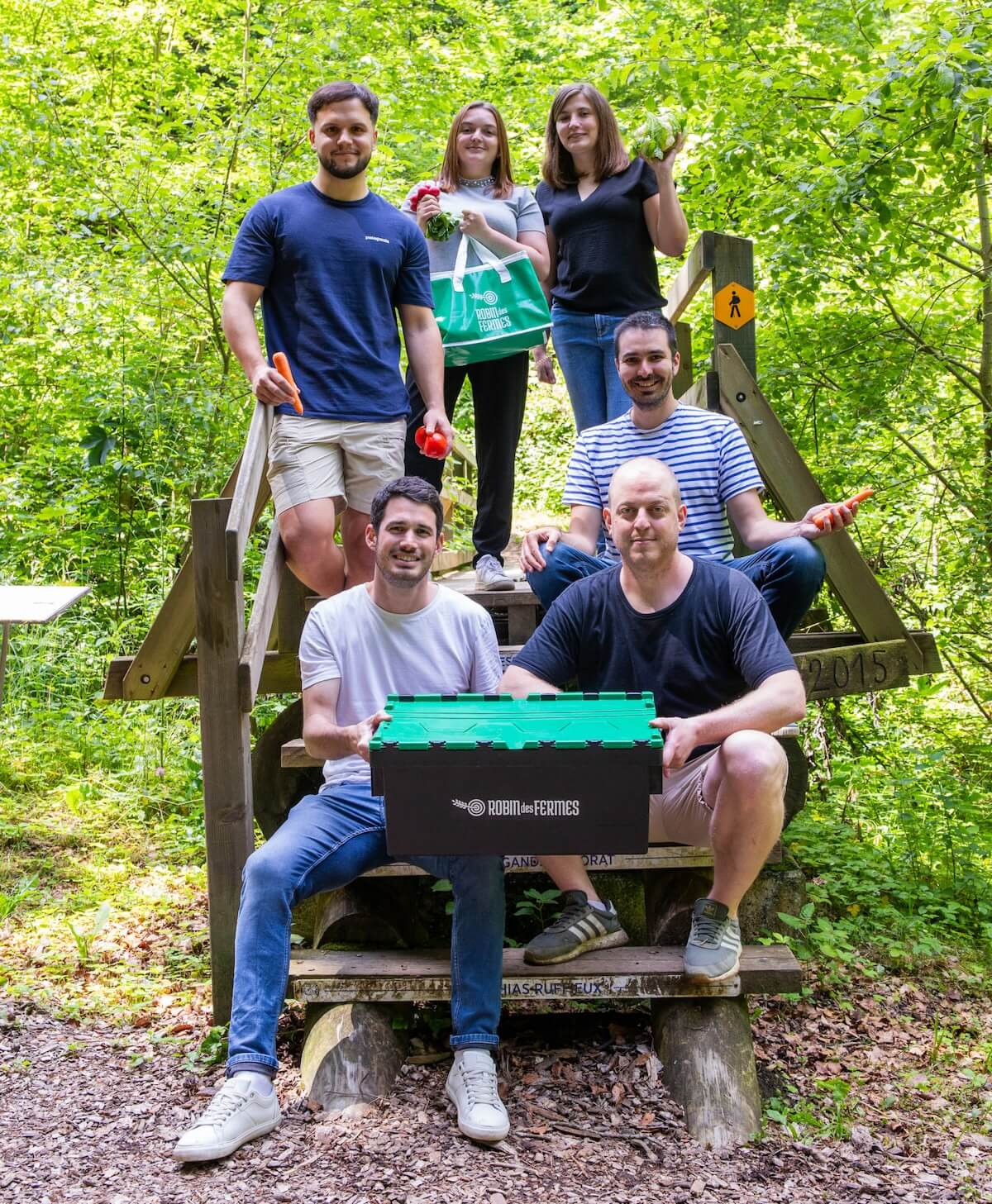 Photo de groupe des membres de l'équipe de Robin des Fermes, posant sur des marches en bois dans une forêt.